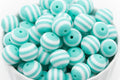 A pile of round, beads with alternating mint green and white horizontal stripes, shown in a white bowl against a white background.