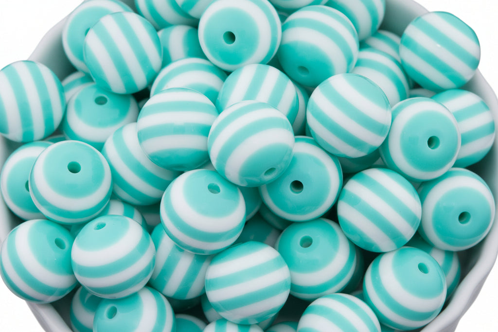 A pile of round, beads with alternating mint green and white horizontal stripes, shown in a white bowl against a white background.