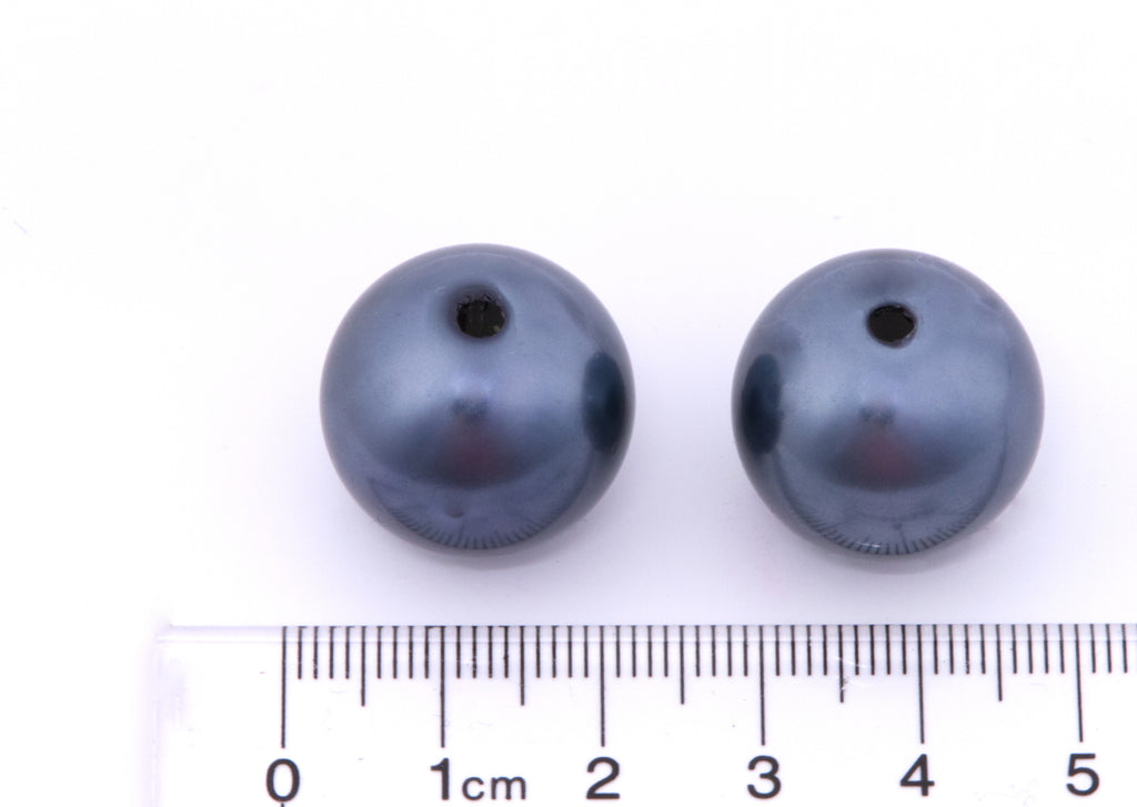Two dark blue mertallic beads with a ruler for scale on a white background