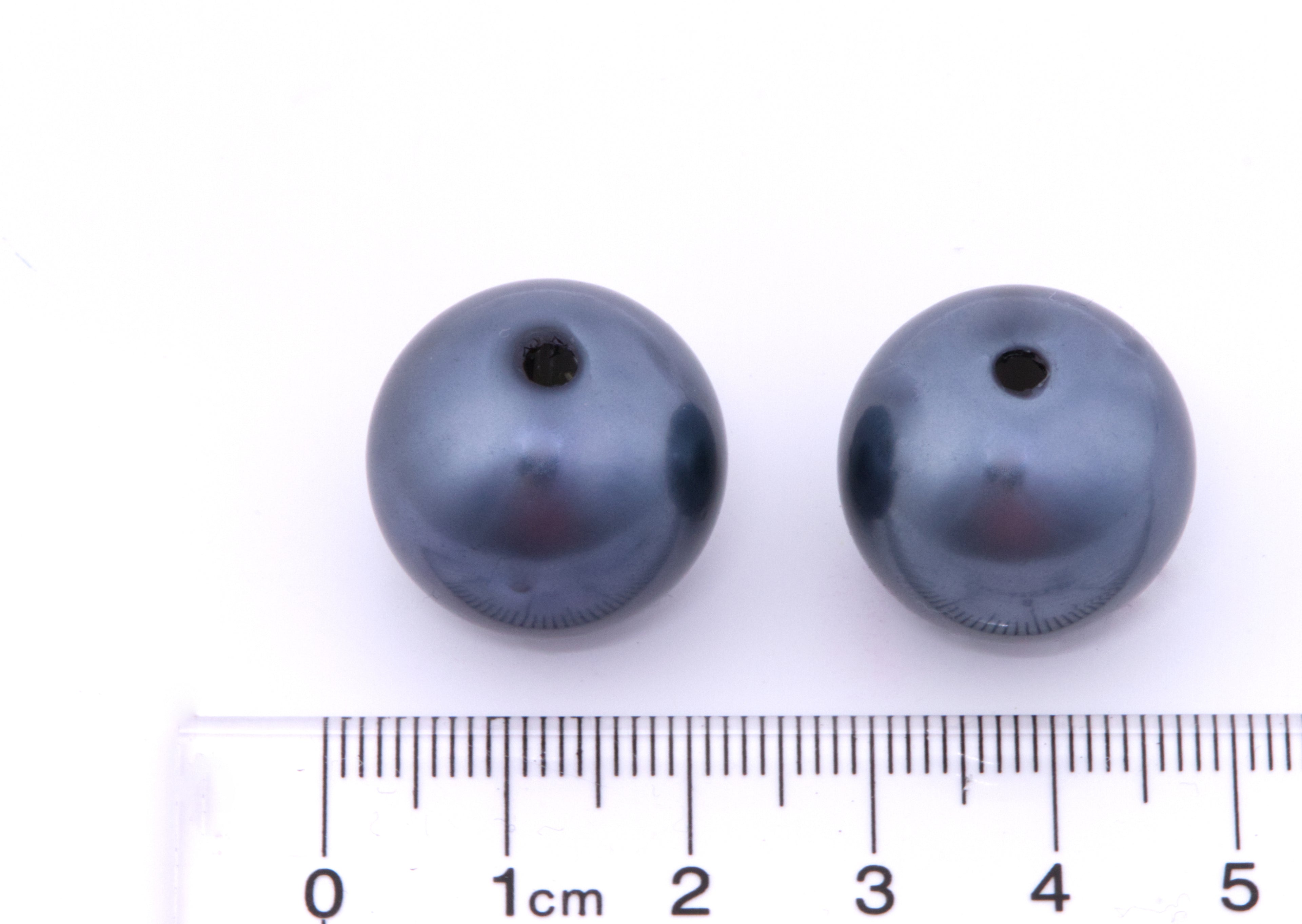 Two dark blue mertallic beads with a ruler for scale on a white background