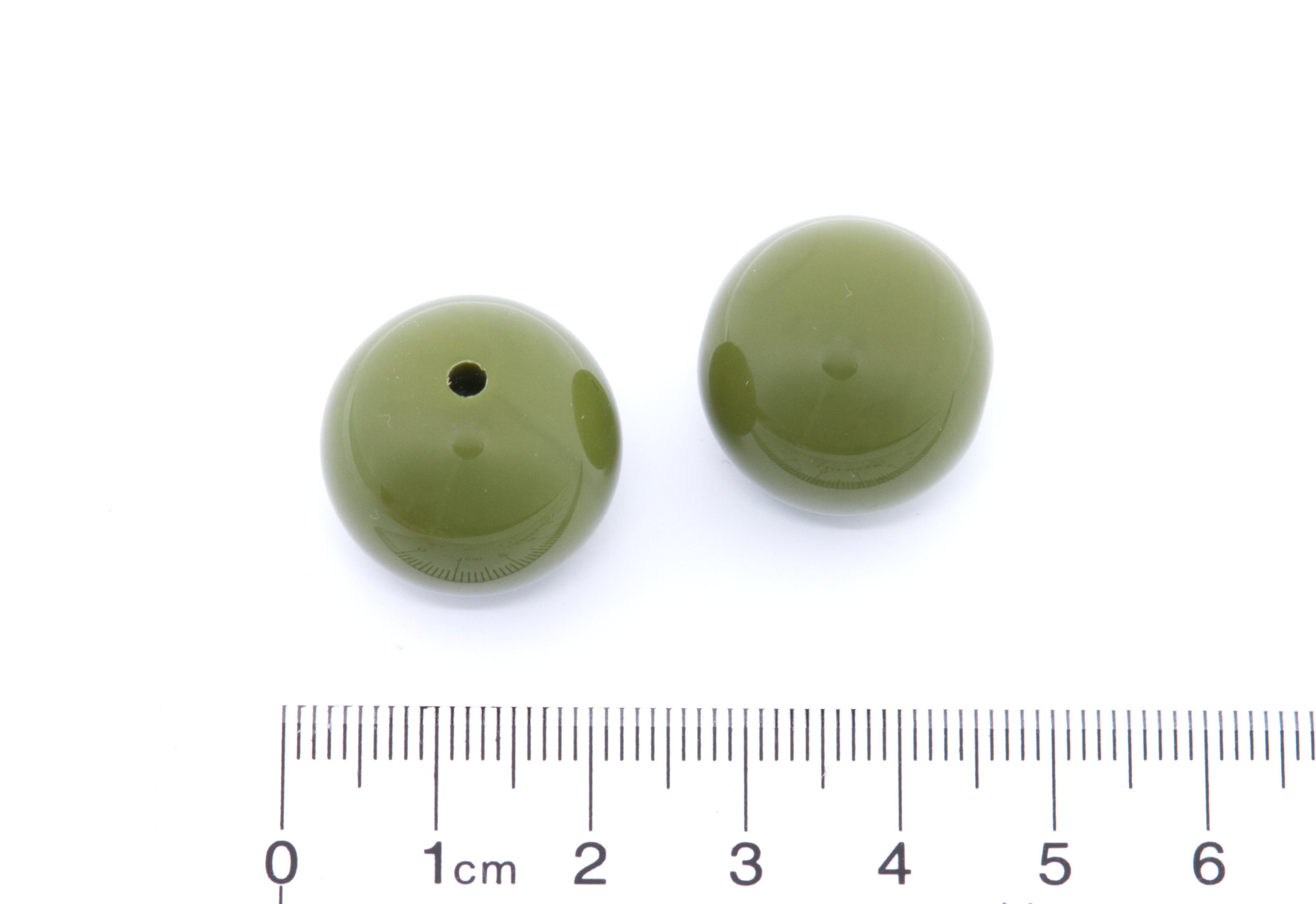 Two green beads with a ruler at the bottom for size reference on a white background