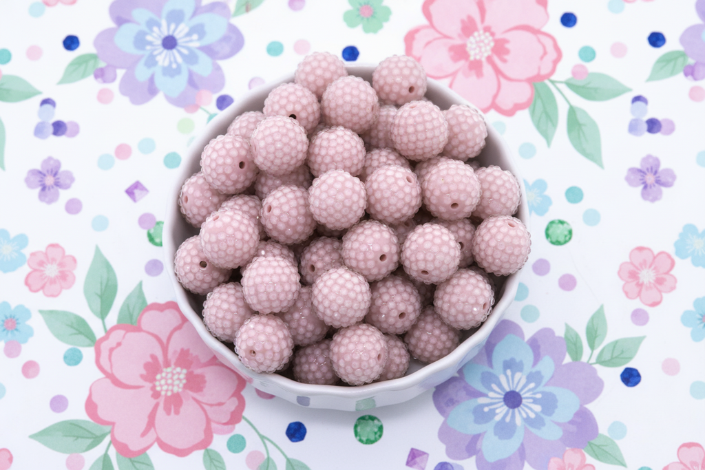 Pink rhinestone beads in a white bowl on a floral patterned background