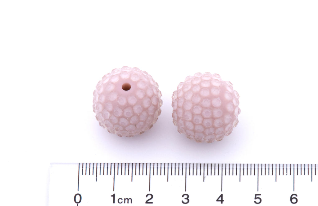 Two pink rhinestone with a ruler for scale on a white background