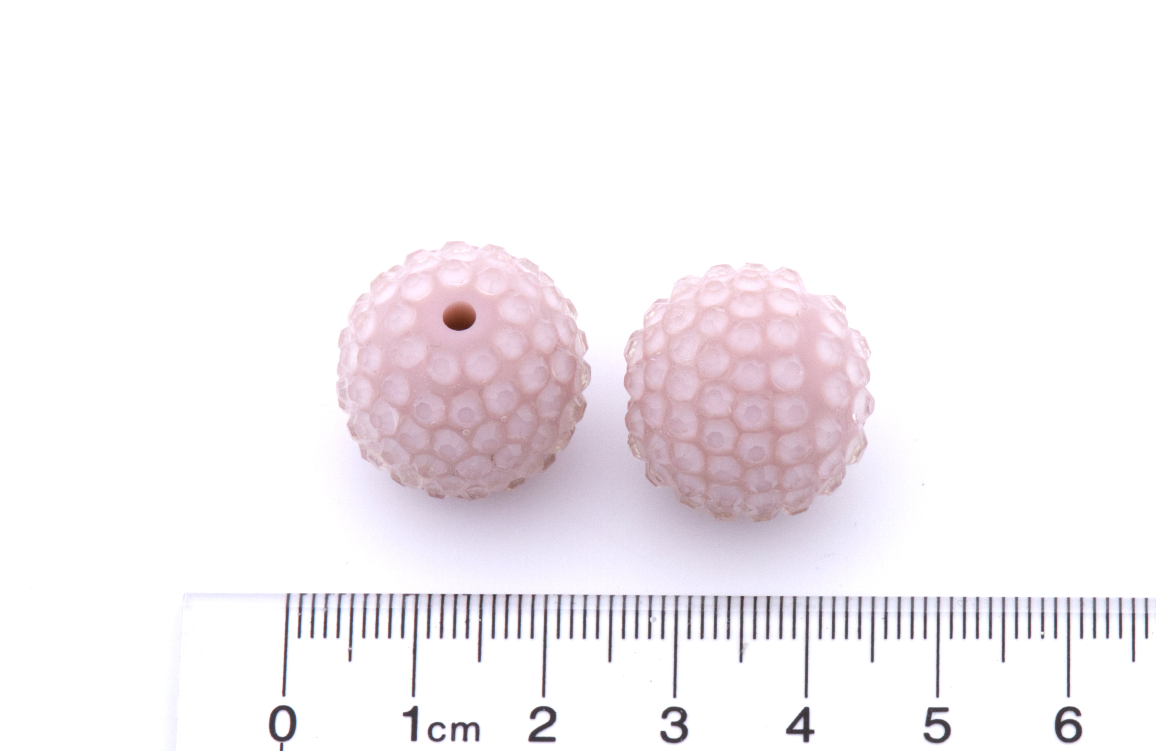 Two pink rhinestone with a ruler for scale on a white background