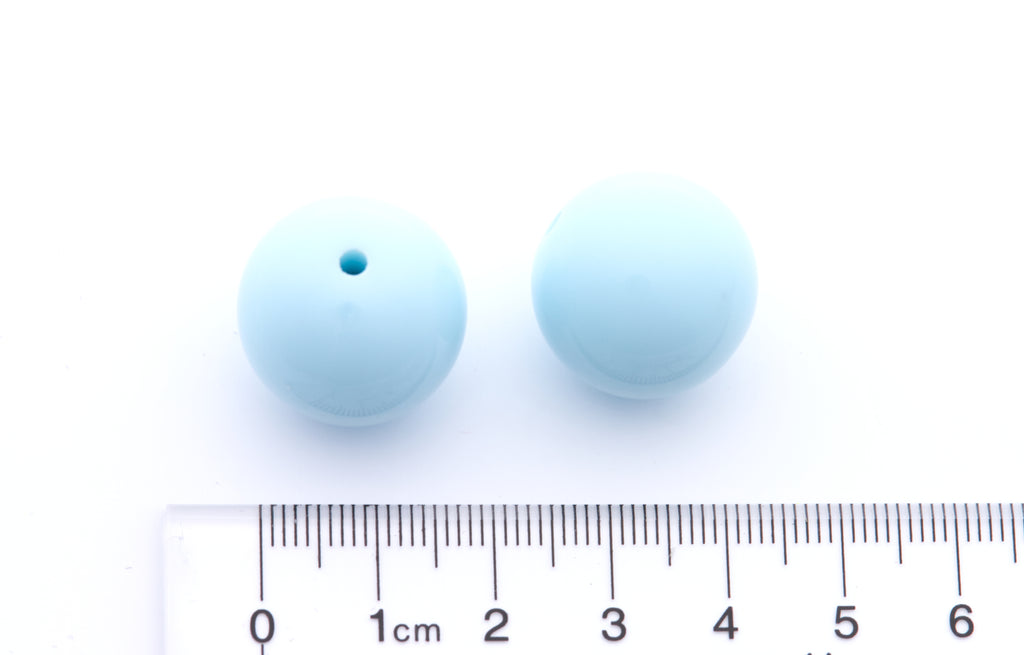 Two light blue beads with a ruler for scale on a white background
