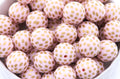 A close-up of round light pink beads with metallic gold polka dots, piled inside a white container.