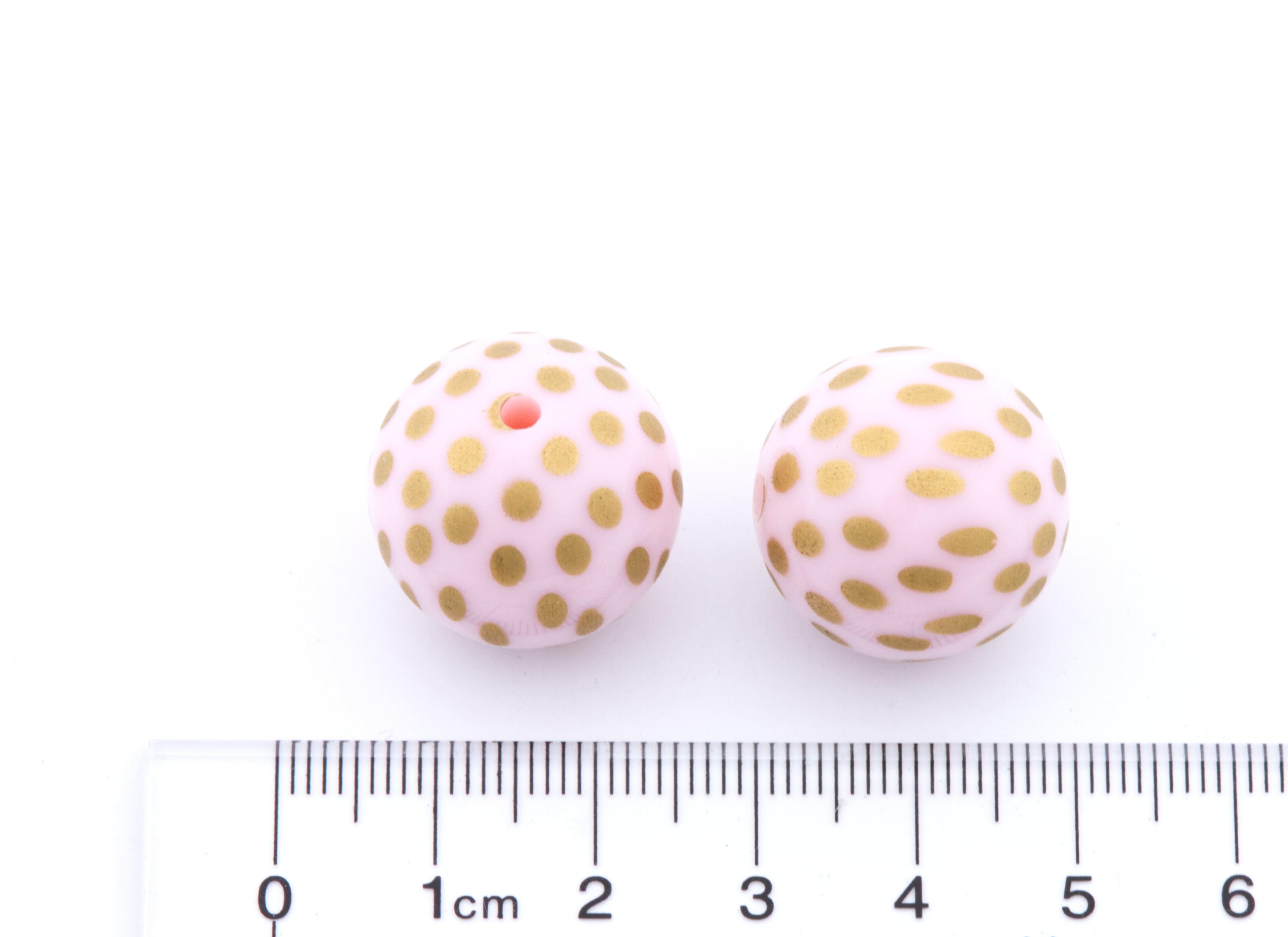 Two round light pink beads with gold polka dots, shown next to a cm ruler for scale on a white background.