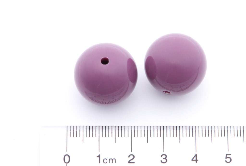 Two purple beads next to a ruler for a scale on a white background