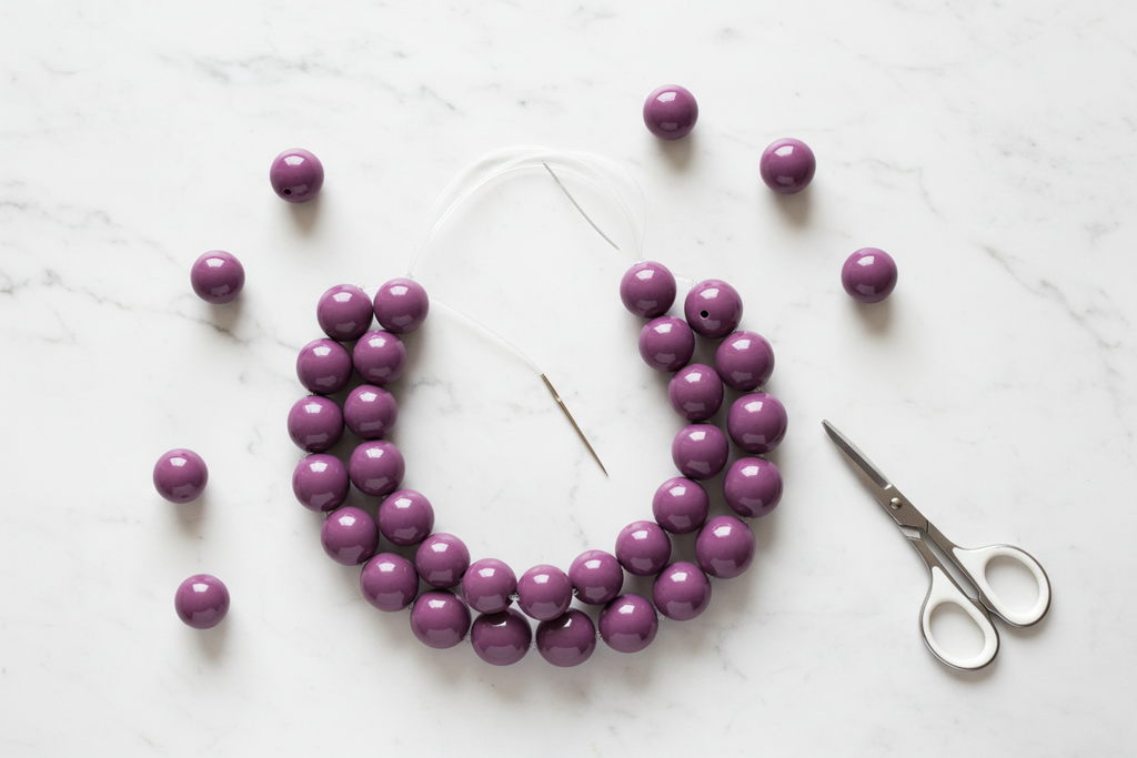 Purple beads shown in a craft with scissors on a white background