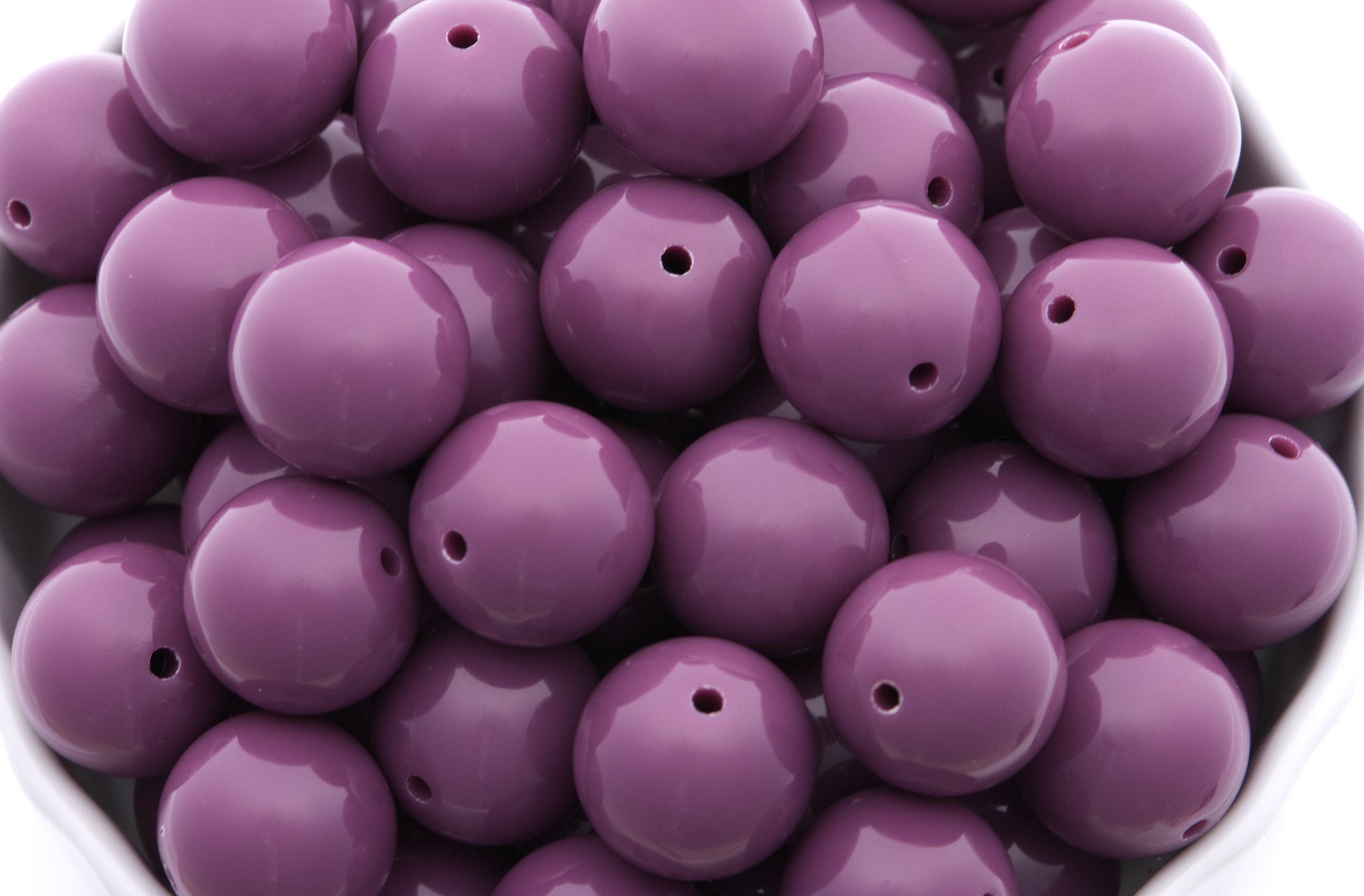 purple beads in a white bowl on a white background