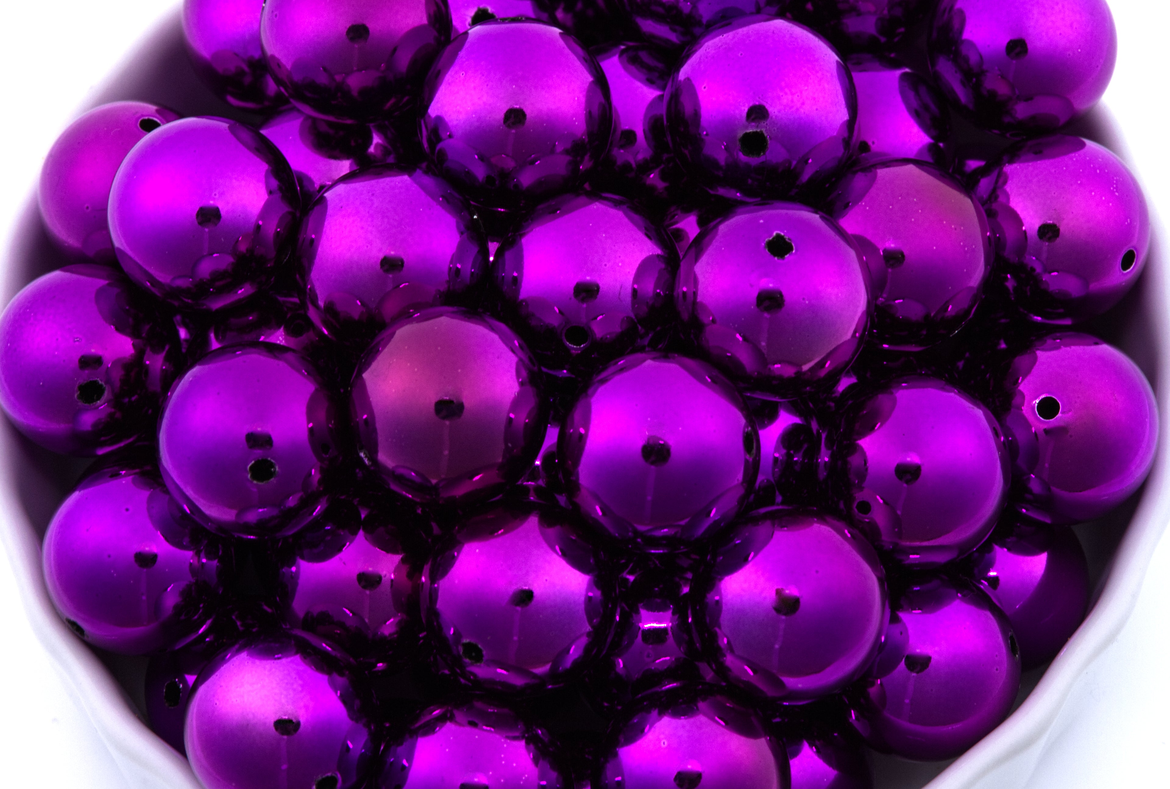 Close-up of purple metallic beads in a white bowl on a white background