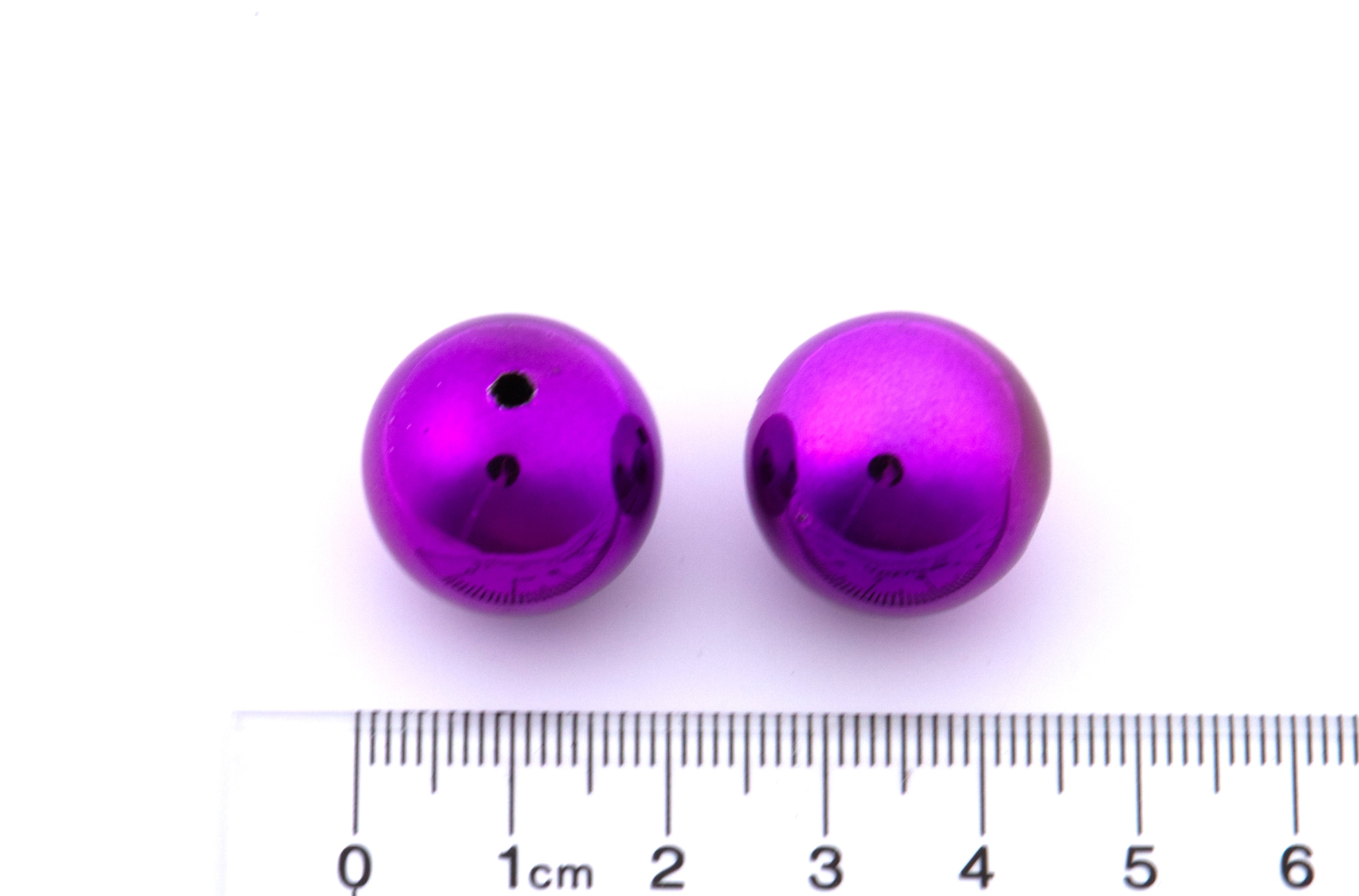 Two purple metallic beads with a ruler for scale on a white background