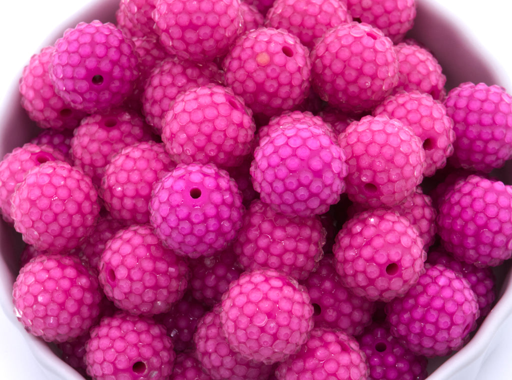 A close-up of bright rhinestone bubblegum beads piled inside a white bowl on a white background. 