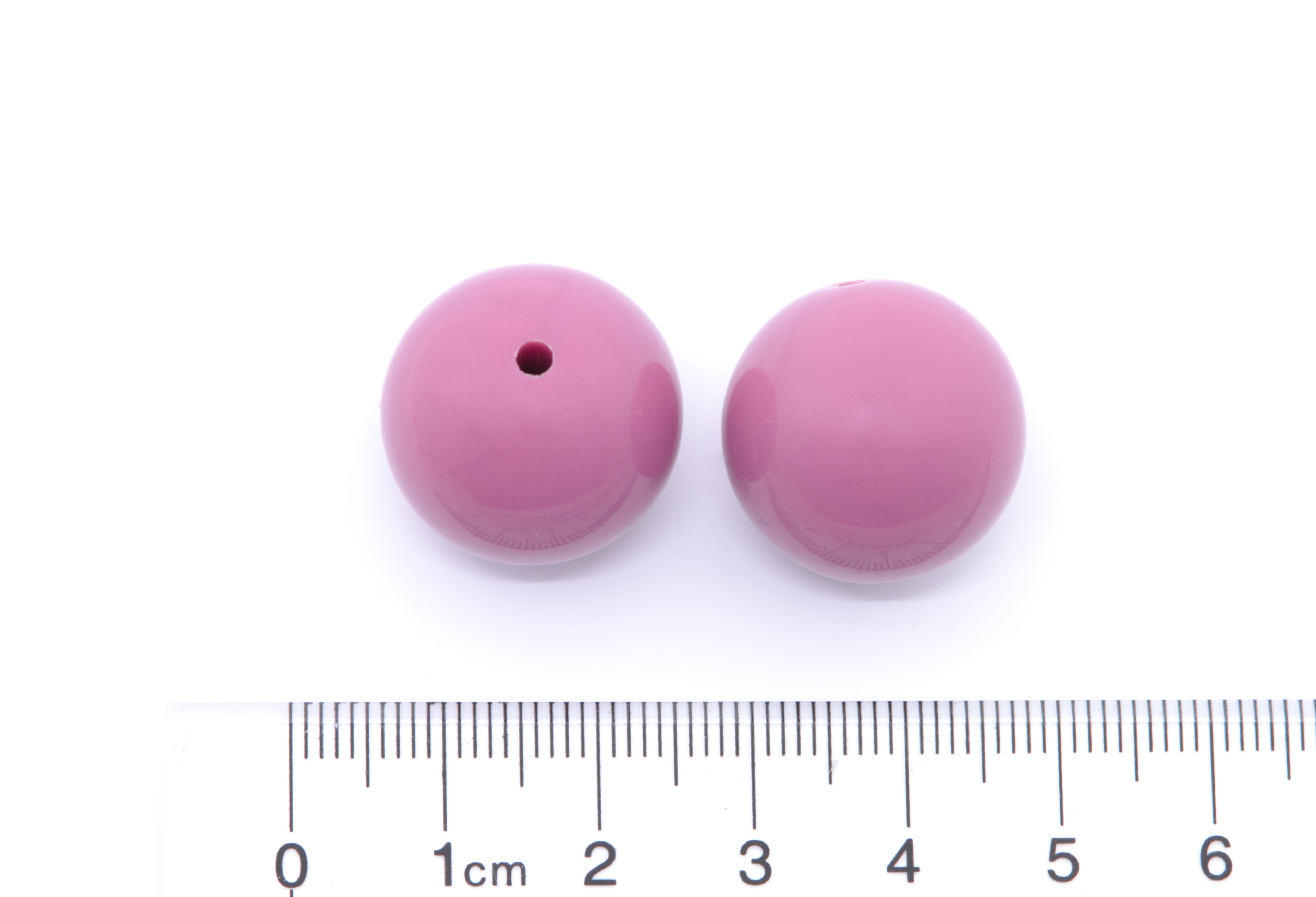 Two purple beads with a ruler for scale on a white background