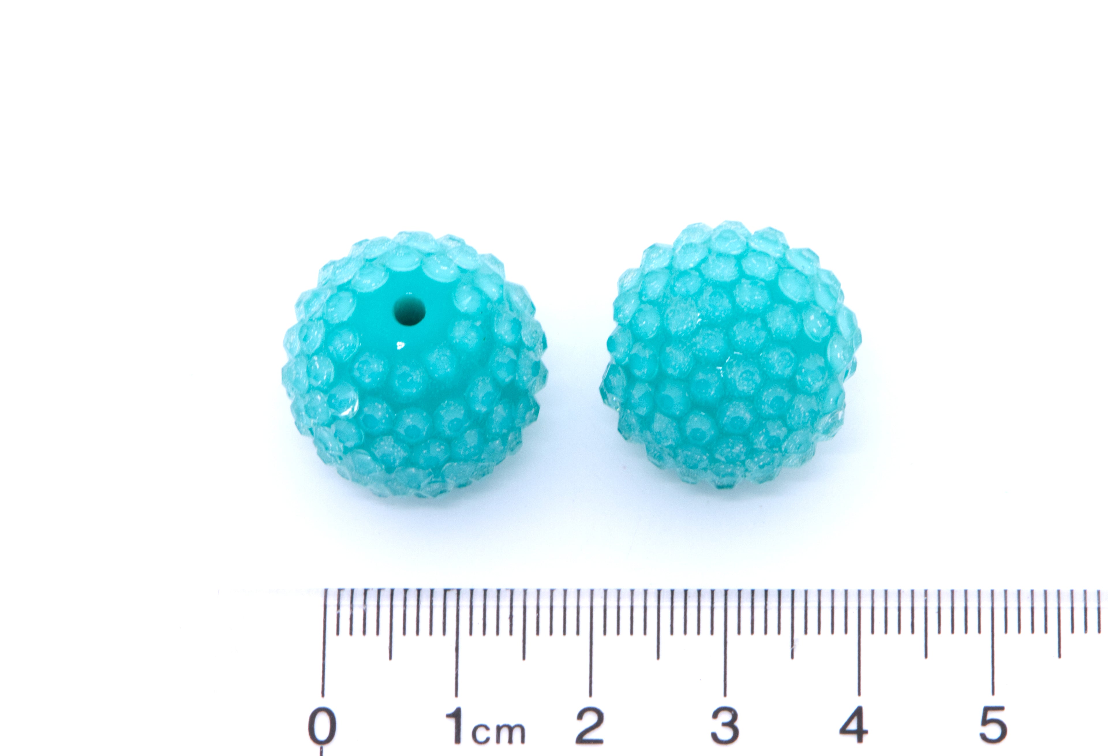 Two teal blue rhinestone bubblegum beads next to a cm ruler for scale on a white background.