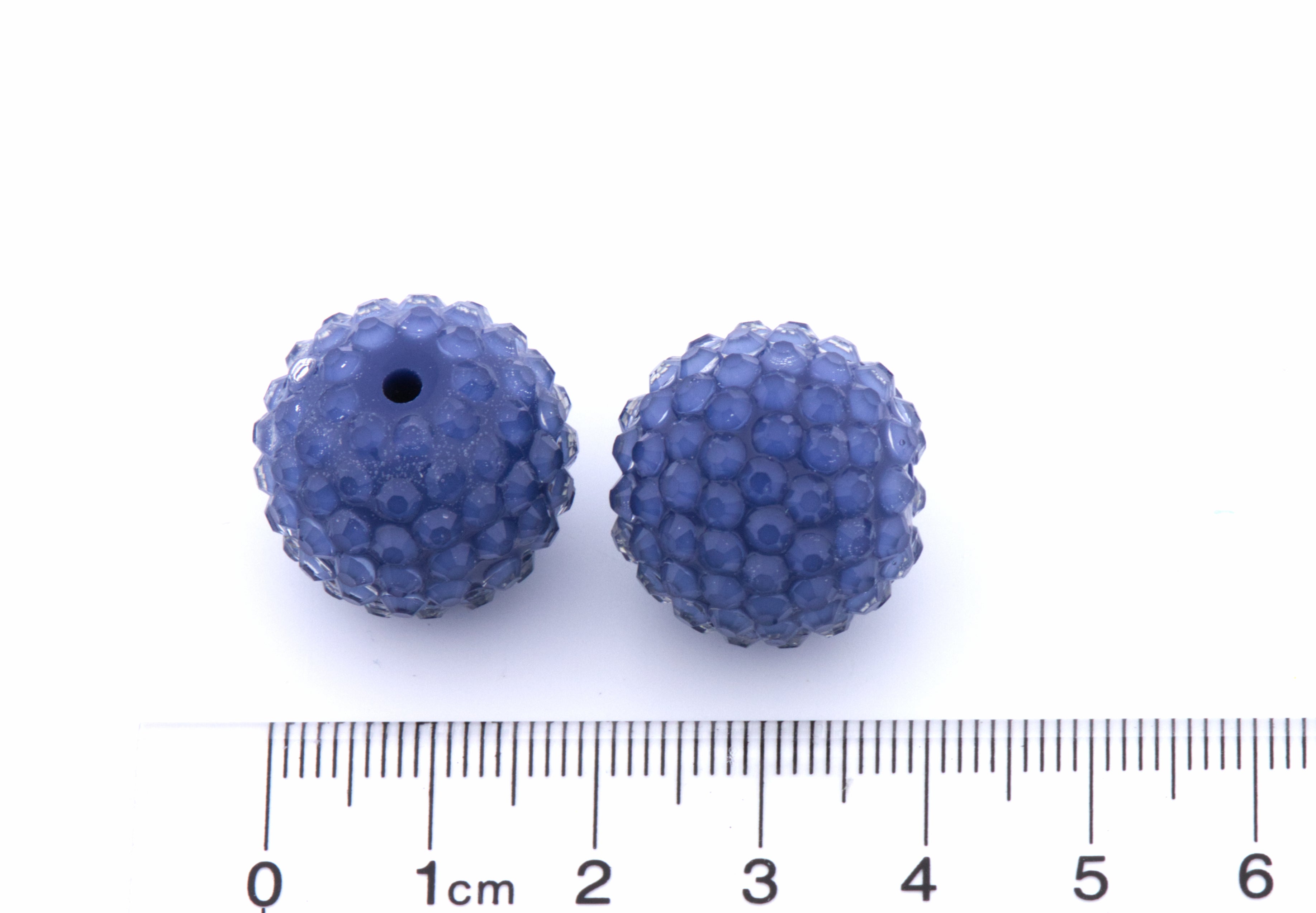 Two blue rhinestone beads shown on a white background with a ruler at the bottom for scale.