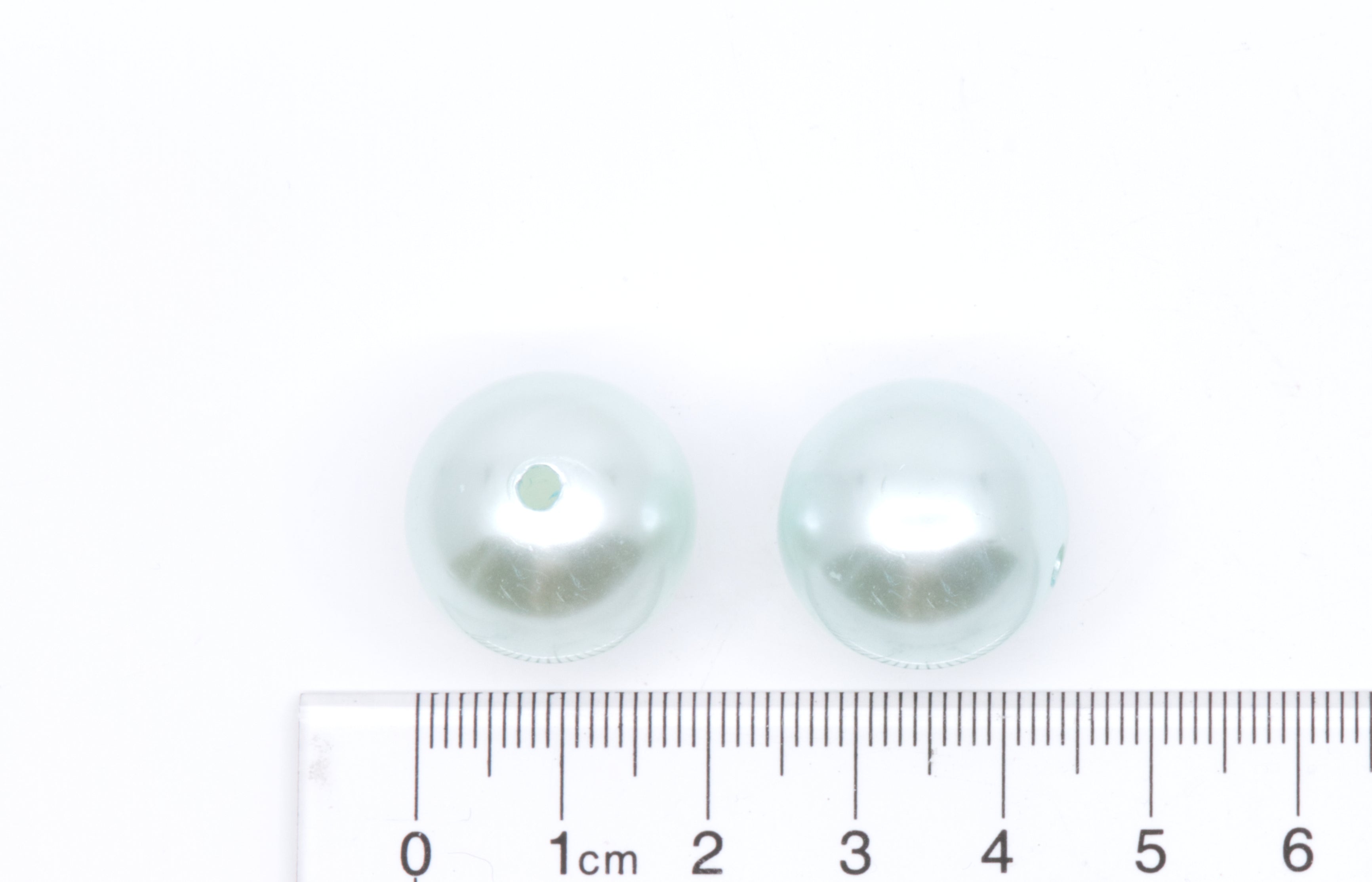 two blue bubblegum beads next to a ruler for scale on a white background