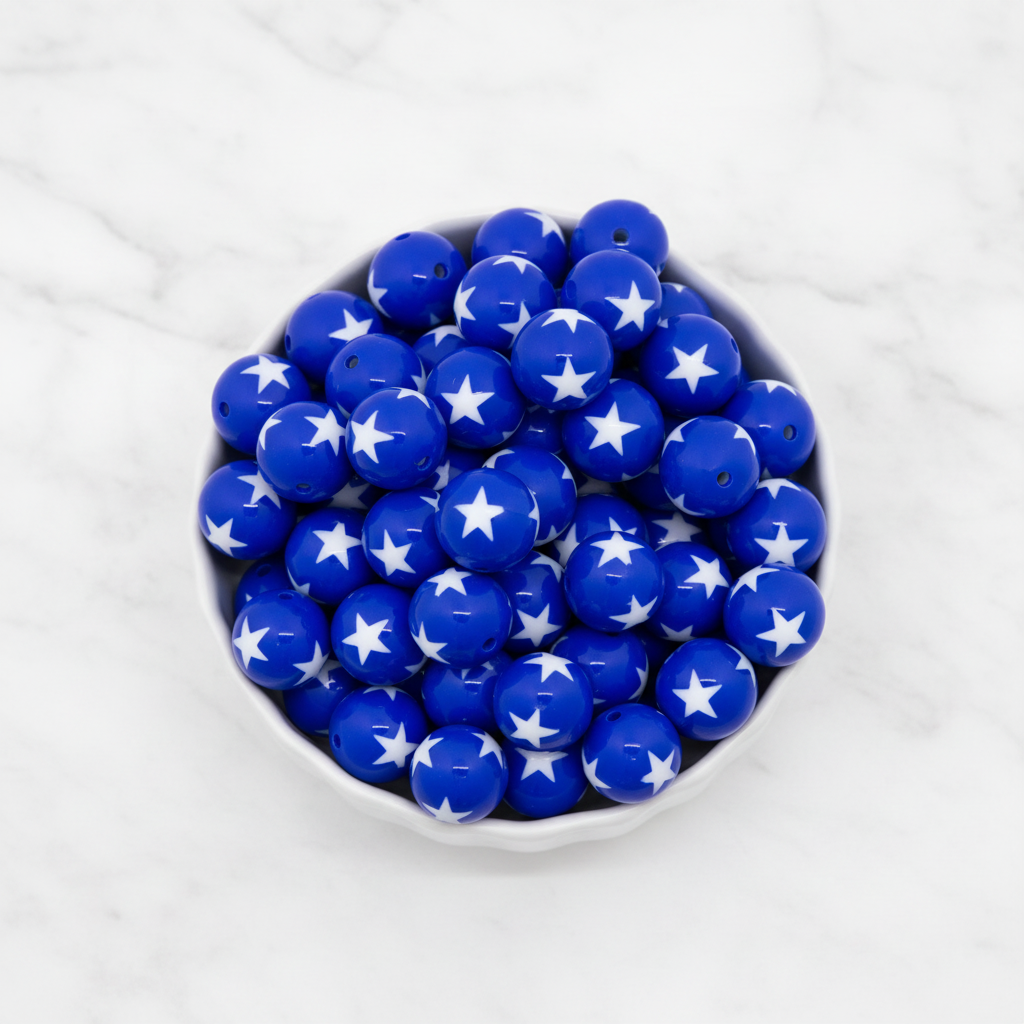 Blue beads with white star patterns in a white bowl on a marble background