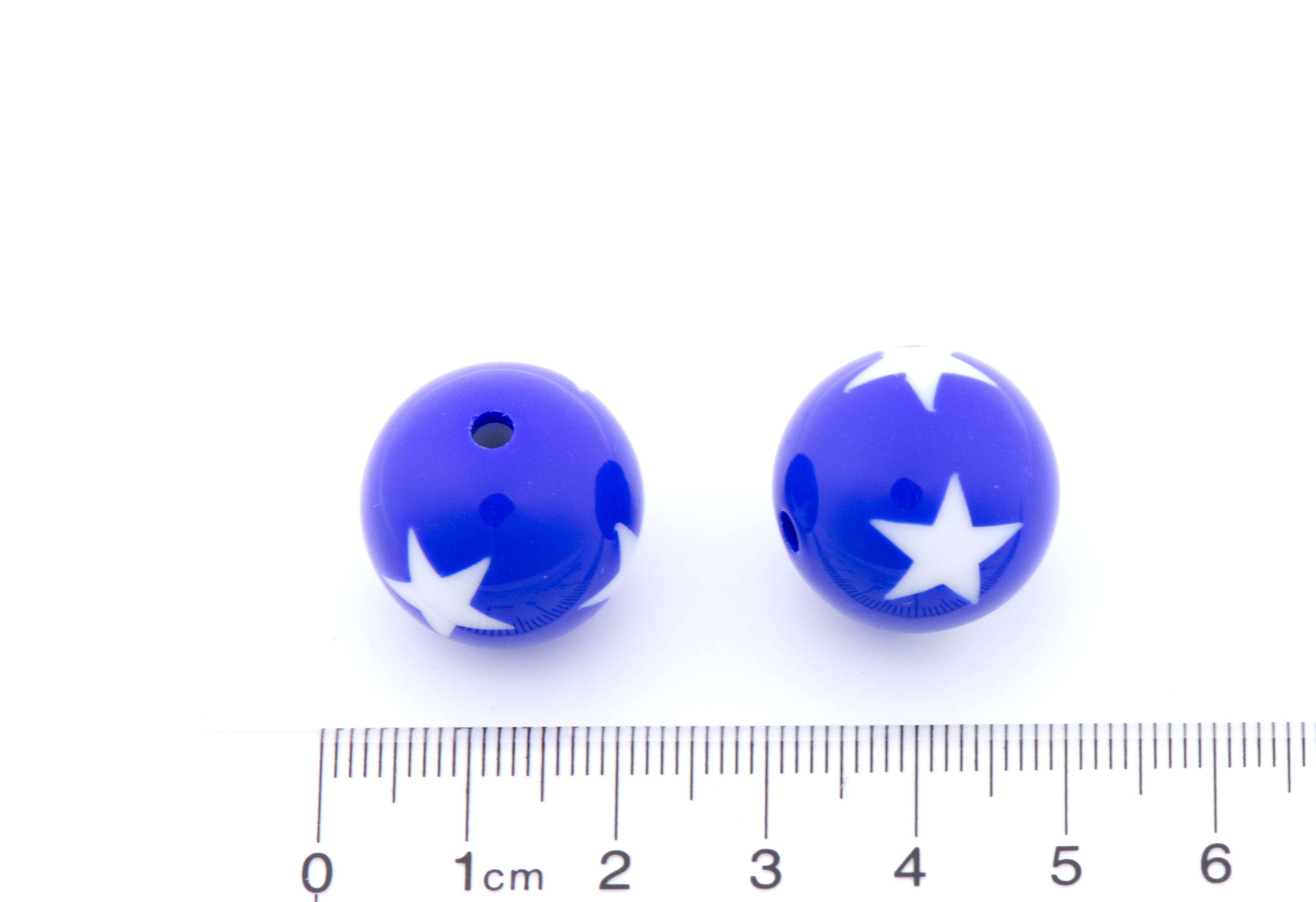 Two blue beads with white stars on a white background, accompanied by a ruler for scale.