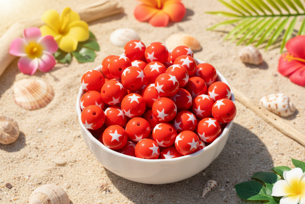 Bowl of red beads with white stars on a sandy background with flowers and shells.