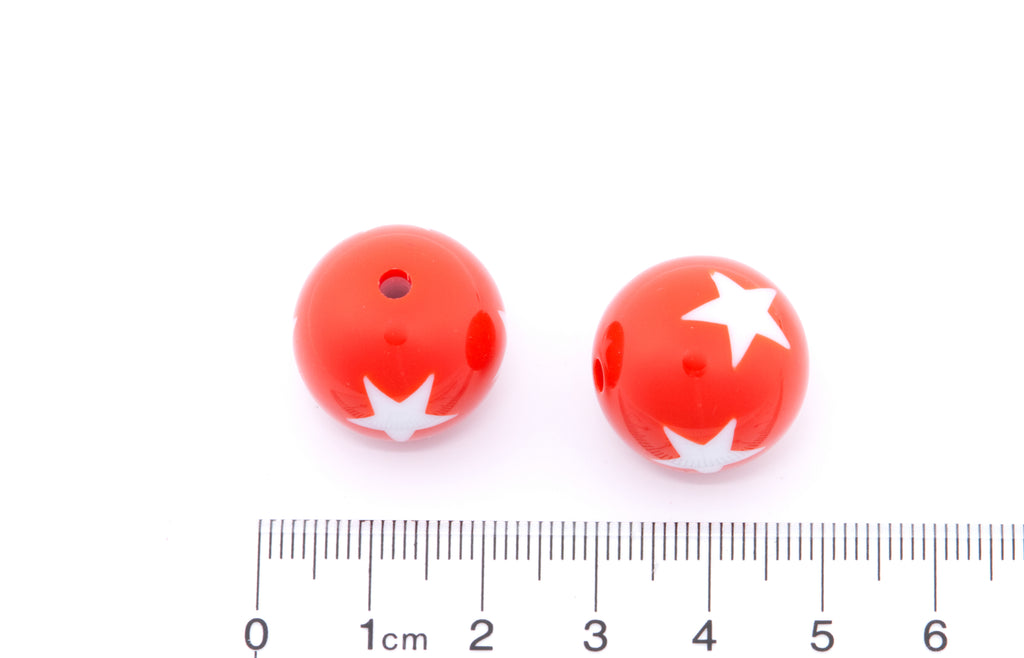 Two red beads with white star patterns on a white background, accompanied by a ruler for scale.