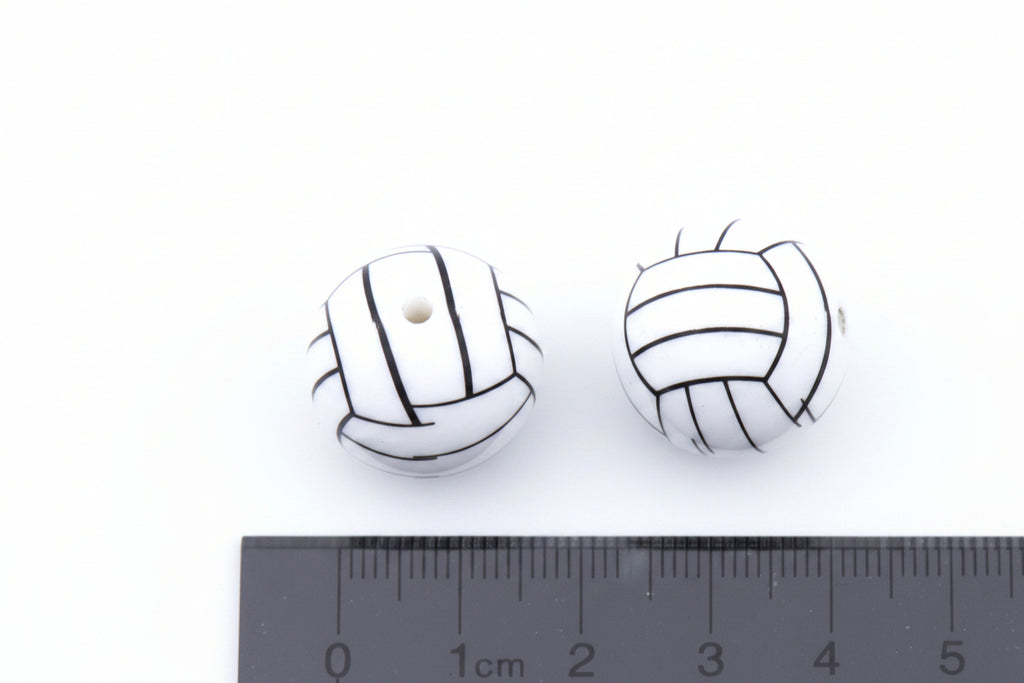 Two white round beads with black volleyball line drawings, shown next to a black cm ruler on a white background.