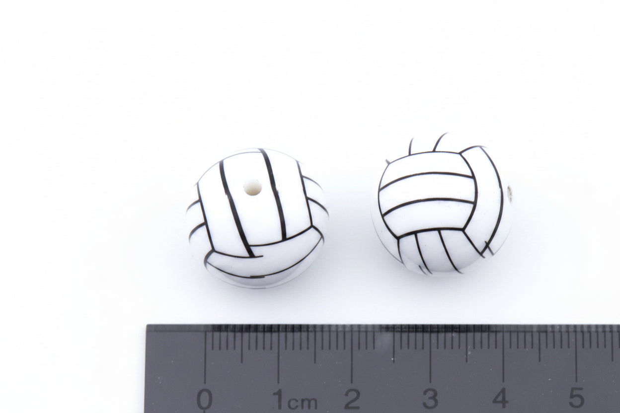 Two white round beads with black volleyball line drawings, shown next to a black cm ruler on a white background.
