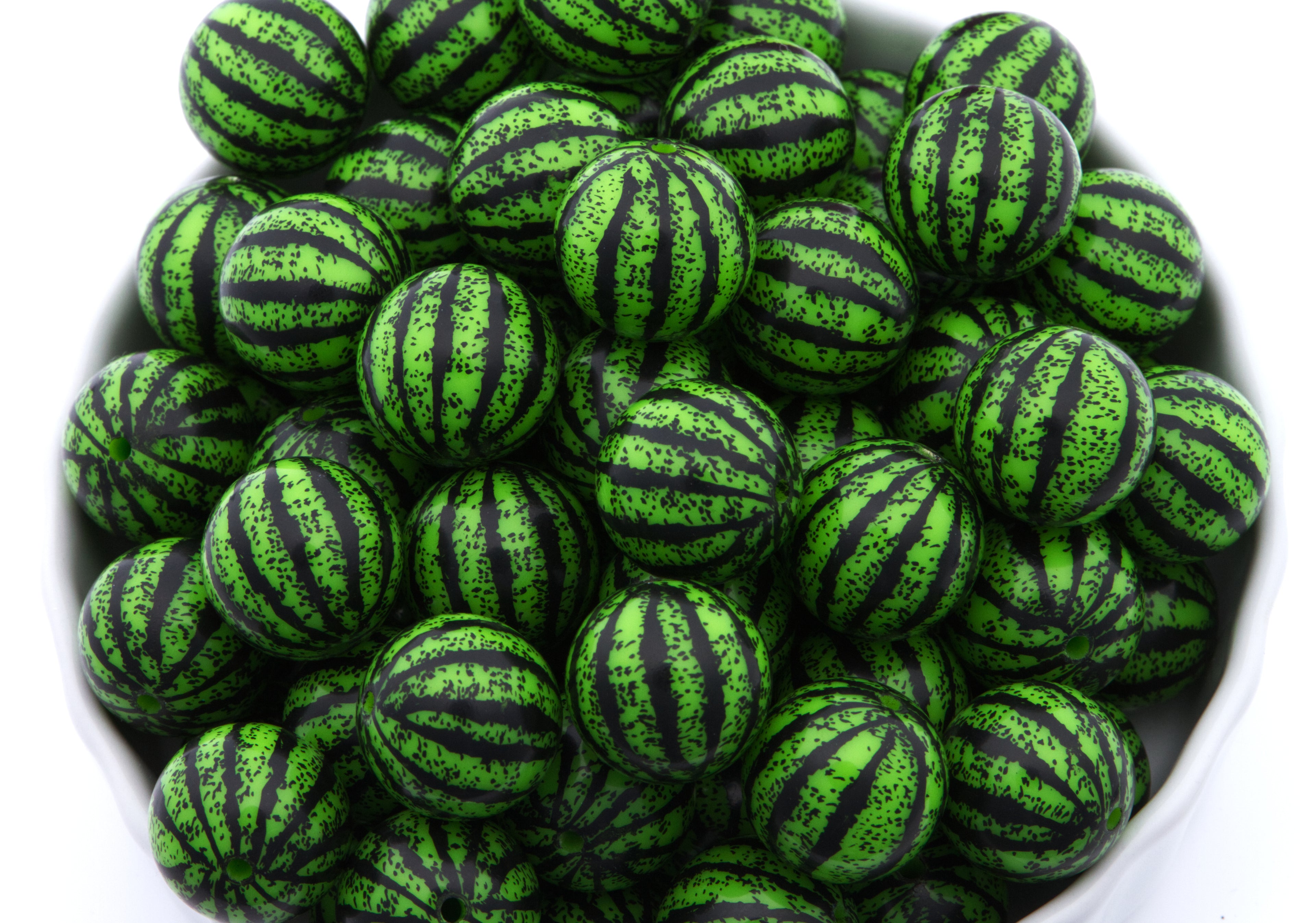 A pile of watermelon striped bubblegum beads displayed in a white bowl against a white background.