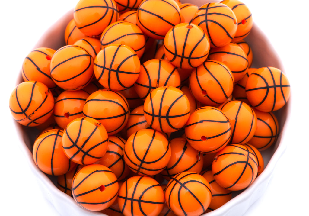 A pile of orange basketball bubblegum beads, arranged inside a white bowl on a white background.