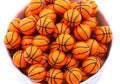 A pile of orange basketball bubblegum beads, arranged inside a white bowl on a white background.