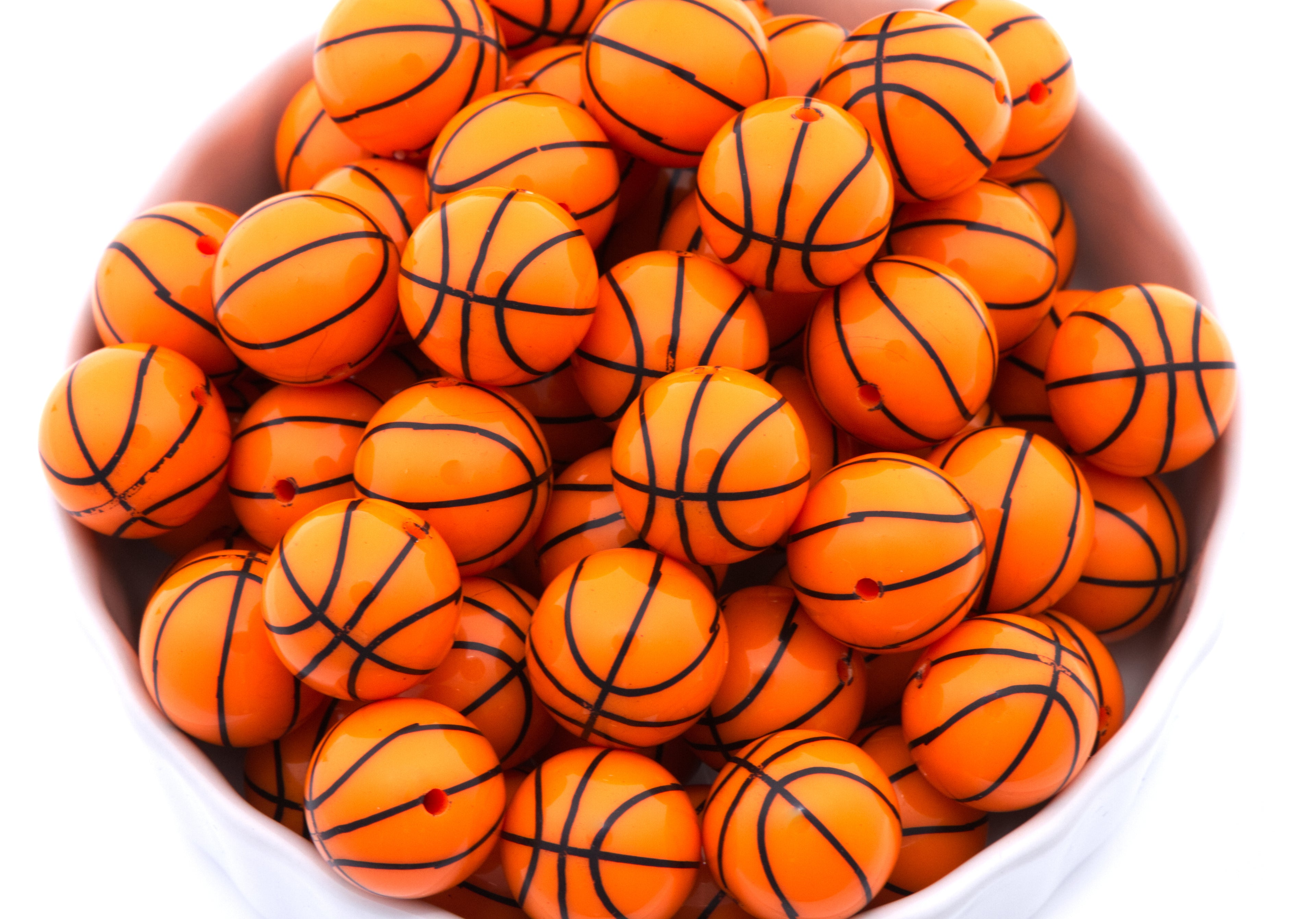 A pile of orange basketball bubblegum beads, arranged inside a white bowl on a white background.
