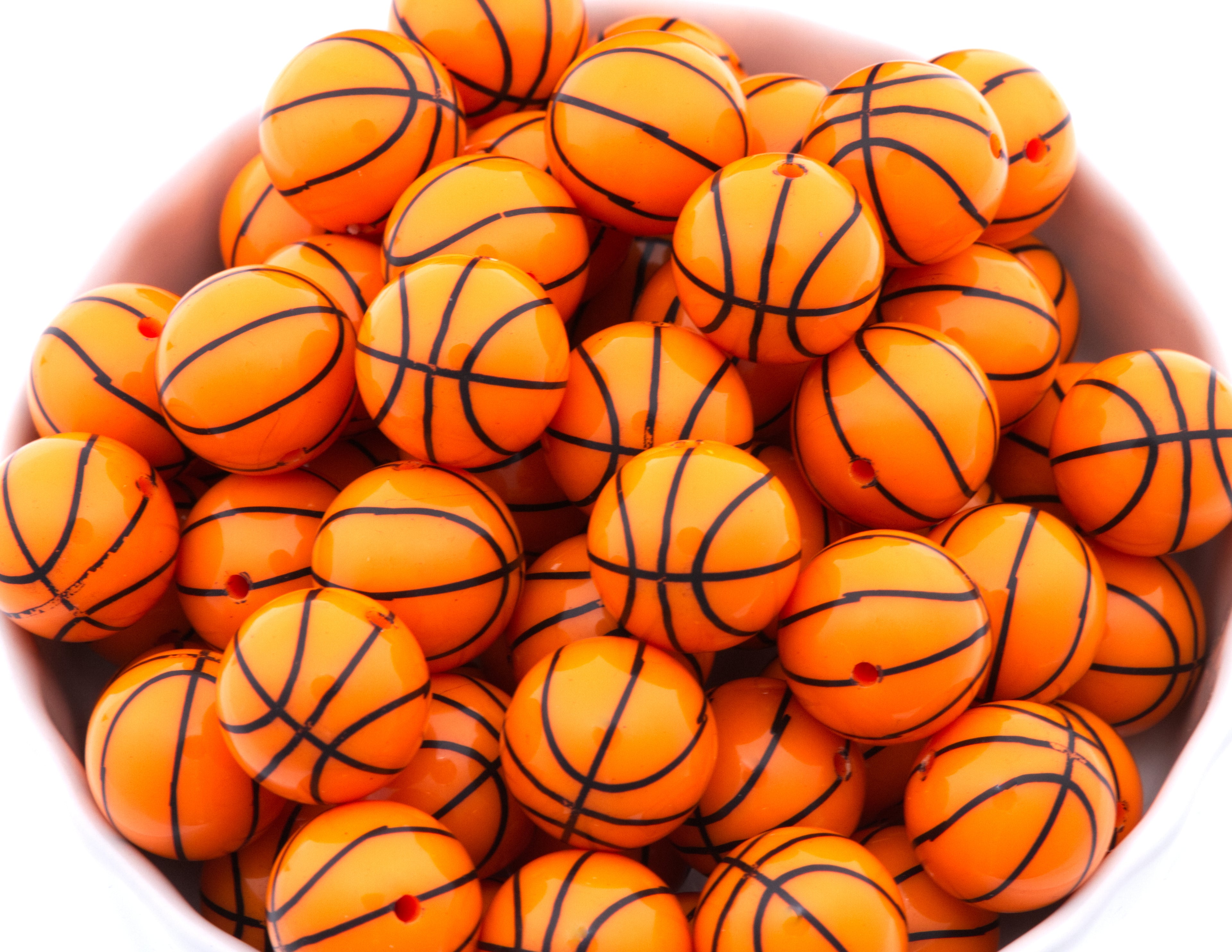 A pile of orange basketball bubblegum beads, arranged inside a white bowl on a white background.