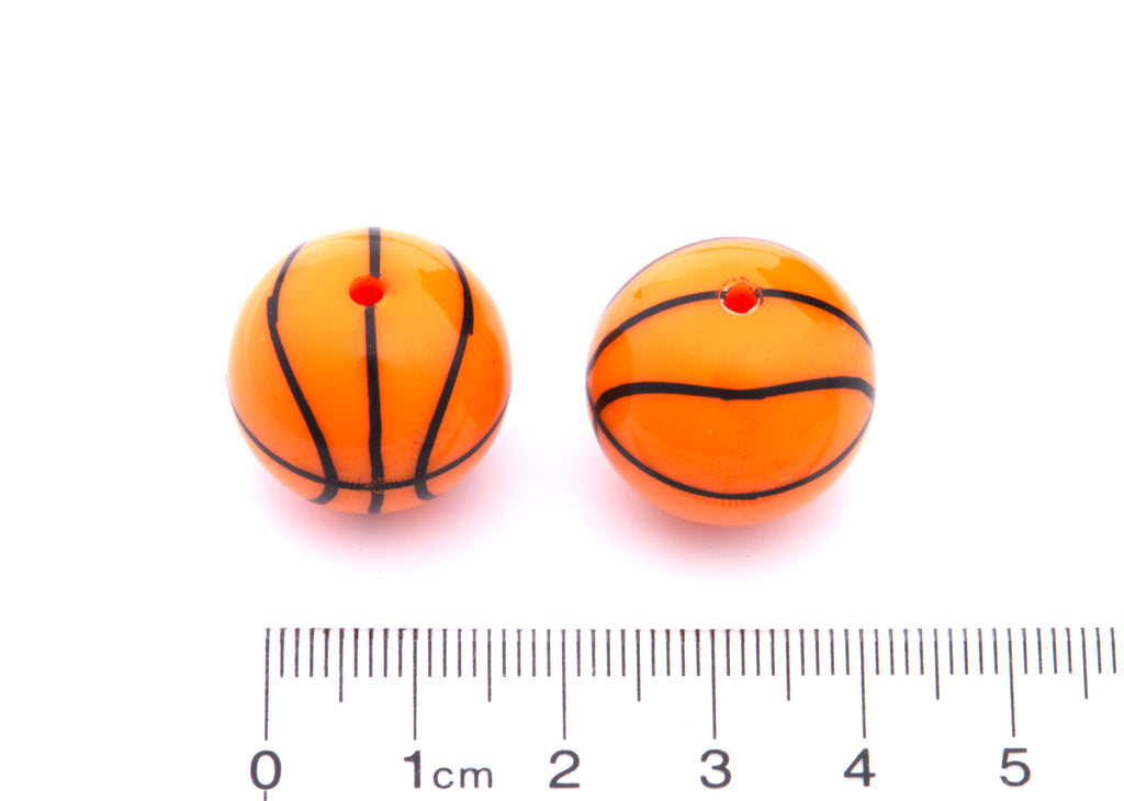 Two orange basketball beads cm ruler for scale on a white background.