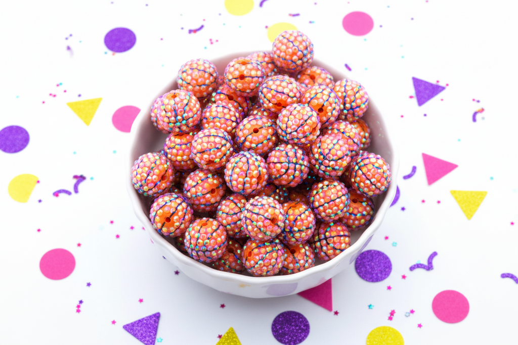 White bowl filled with rhinestone basketball beads on a white background with colorful confetti.