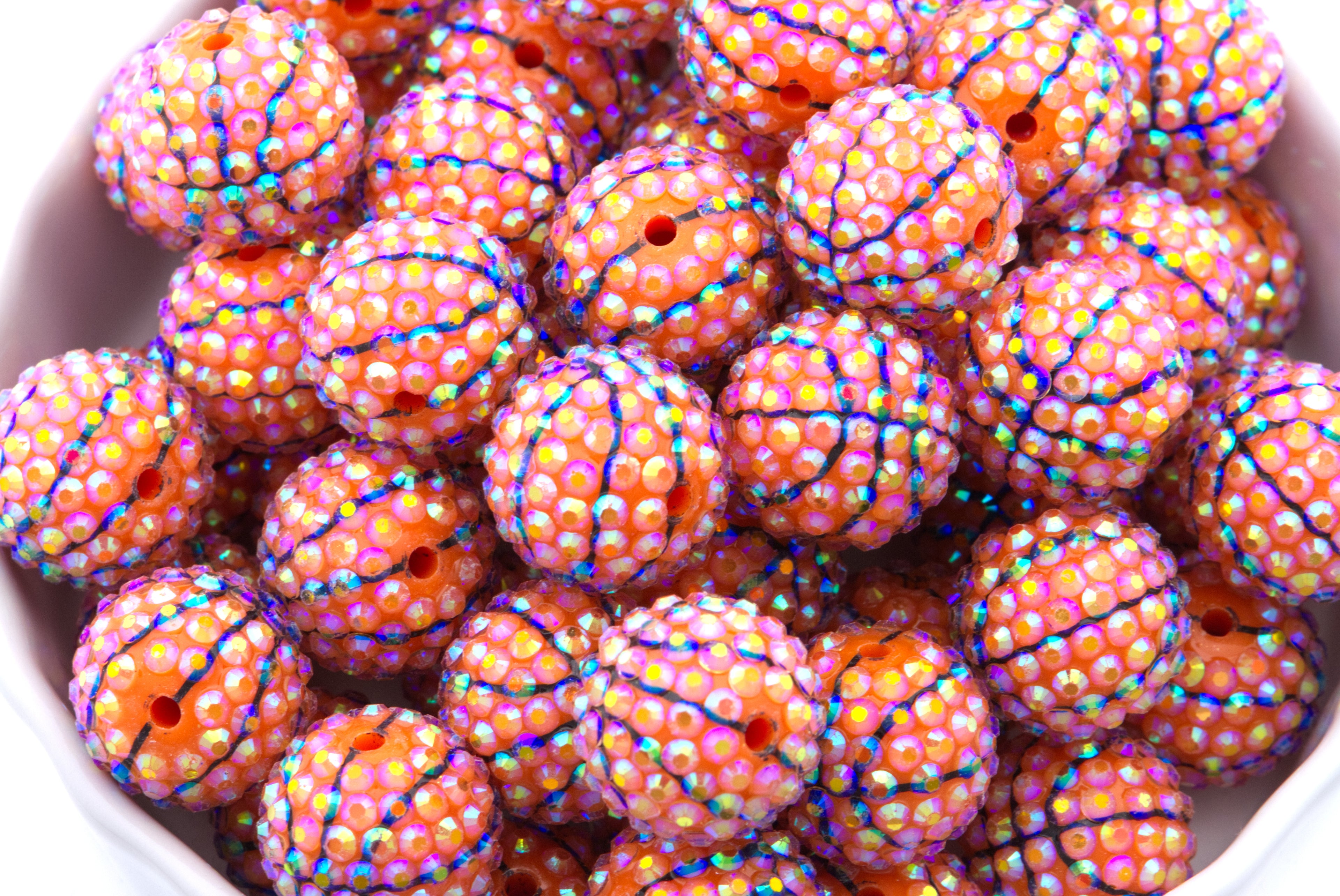 Colorful basketball rhinestone beads in a white bowl on a white background 