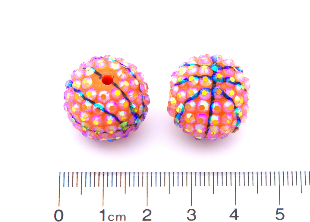 Two colorful basketball rhinestone beads with a ruler for scale on a white background