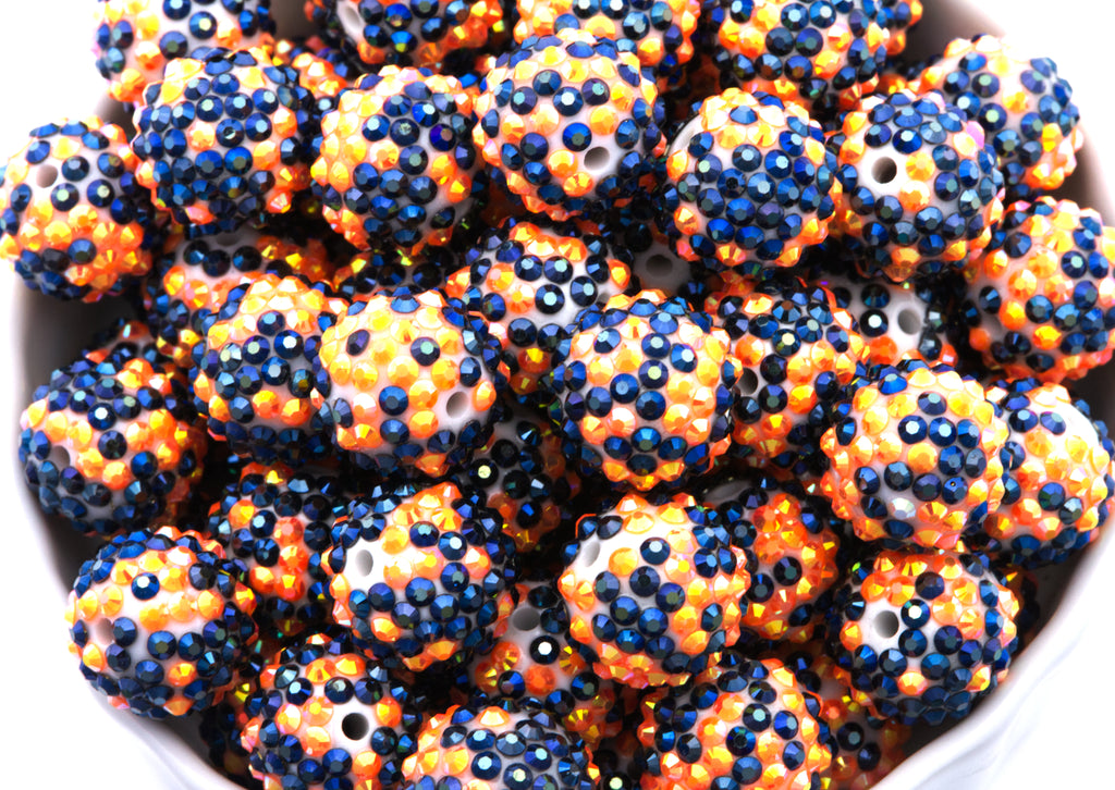 A close-up of many black and orange rhinestone beads filling a white bowl against a white background.
