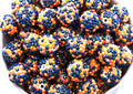 A close-up of many black and orange rhinestone beads filling a white bowl against a white background.