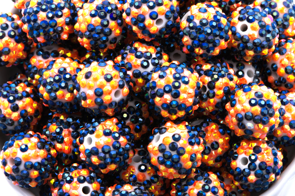 A close-up of many black and orange rhinestone beads filling a white bowl against a white background.
