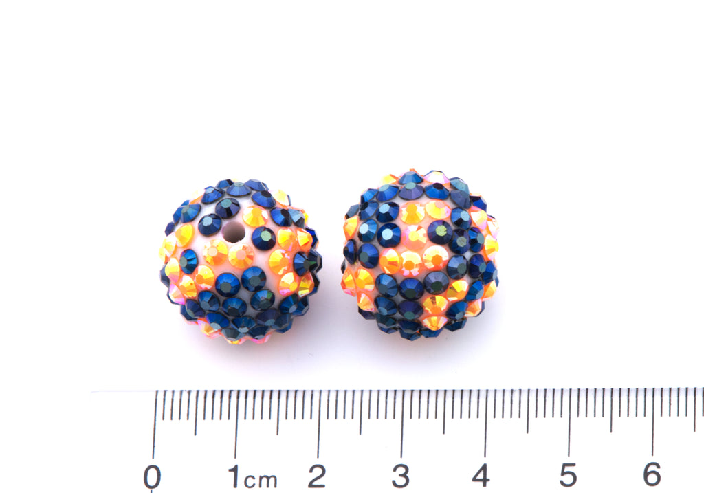 Two round orange and black rhinestone beads, shown next to a cm ruler for scale on a white background.