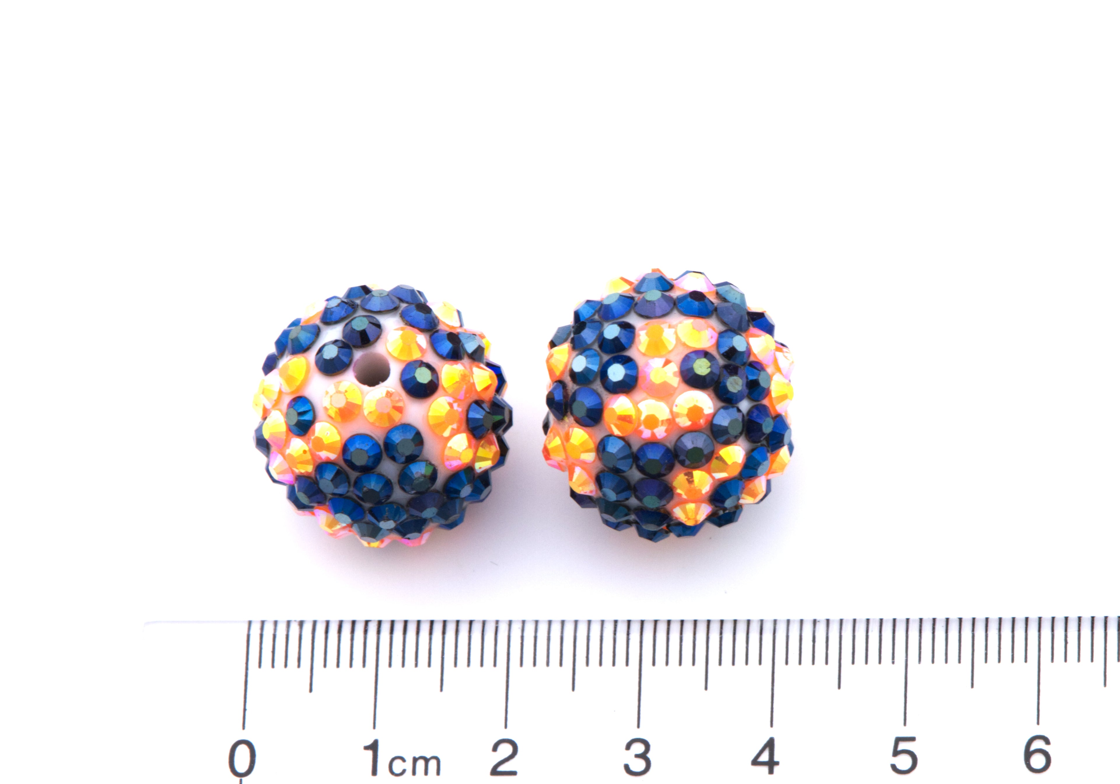 Two round orange and black rhinestone beads, shown next to a cm ruler for scale on a white background.