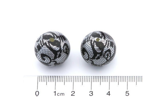 Two round black and Silver lace patterned beads shown next to a cm ruler for scale on a white background.