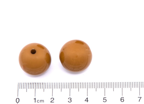 Two brown beads with a ruler at the bottom for scale on a white background