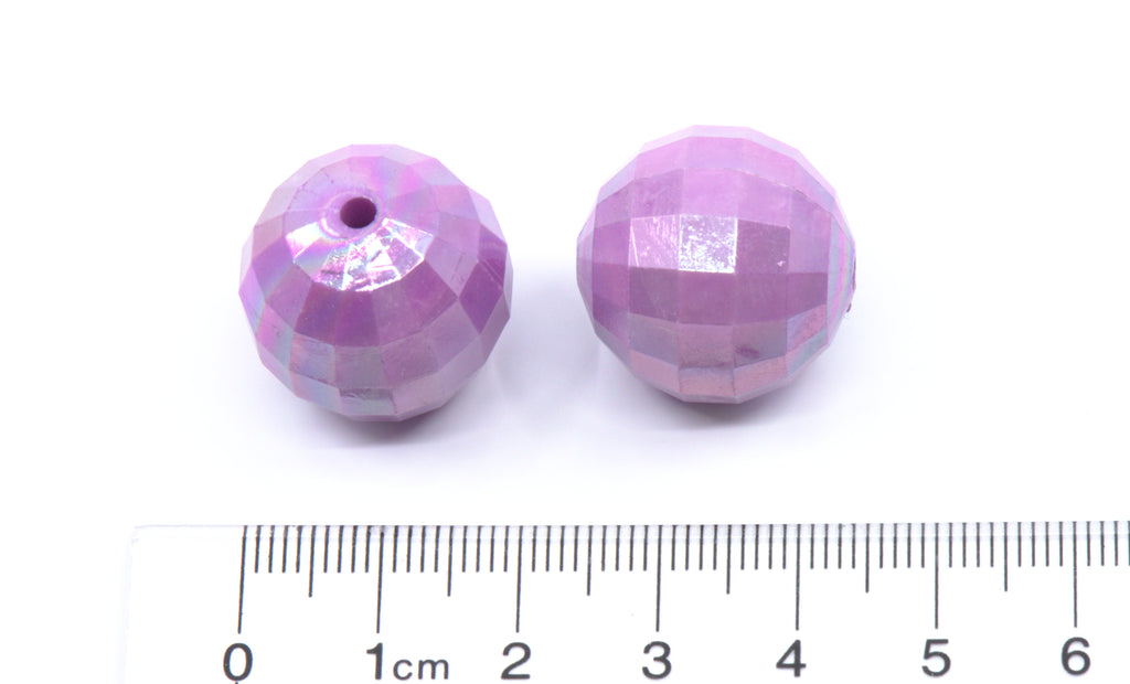 Two purple faceted beads with a ruler for scale on a white background