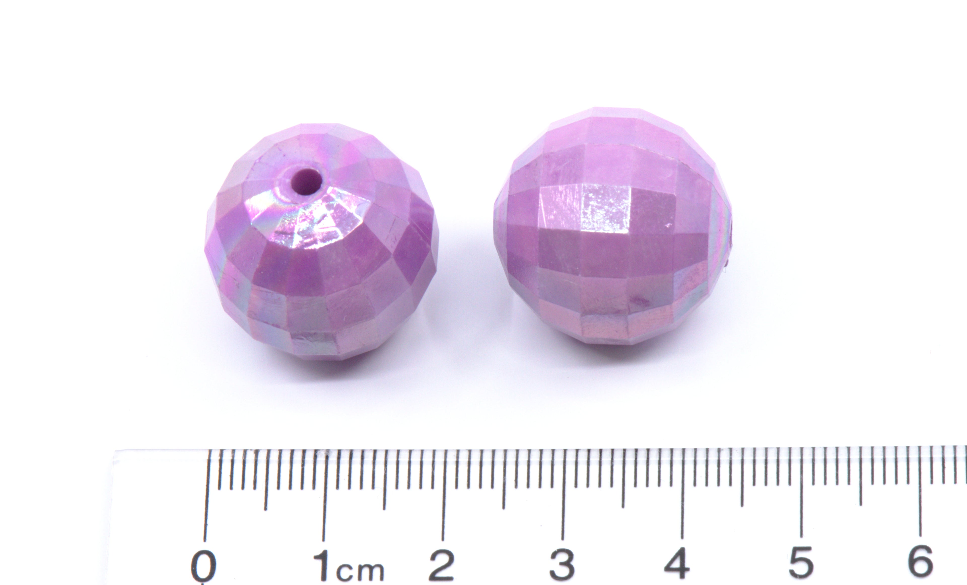 Two purple faceted beads with a ruler for scale on a white background