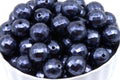 A pile of faceted dark blue bubblegum beads displayed in a white bowl against a white background.