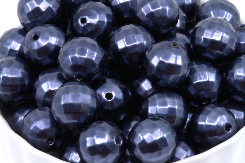 A pile of faceted dark blue bubblegum beads displayed in a white bowl against a white background.