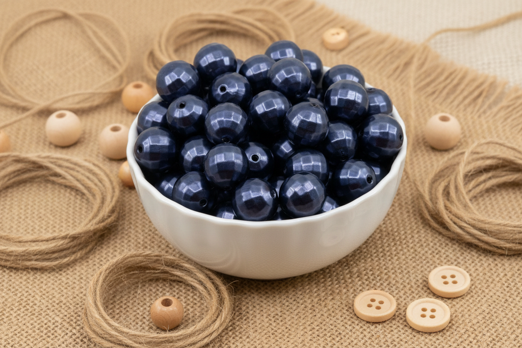 A white ceramic bowl filled with dark blue faceted beads, arranged on a burlap surface with loose twine, wooden buttons, and small wooden beads around it.