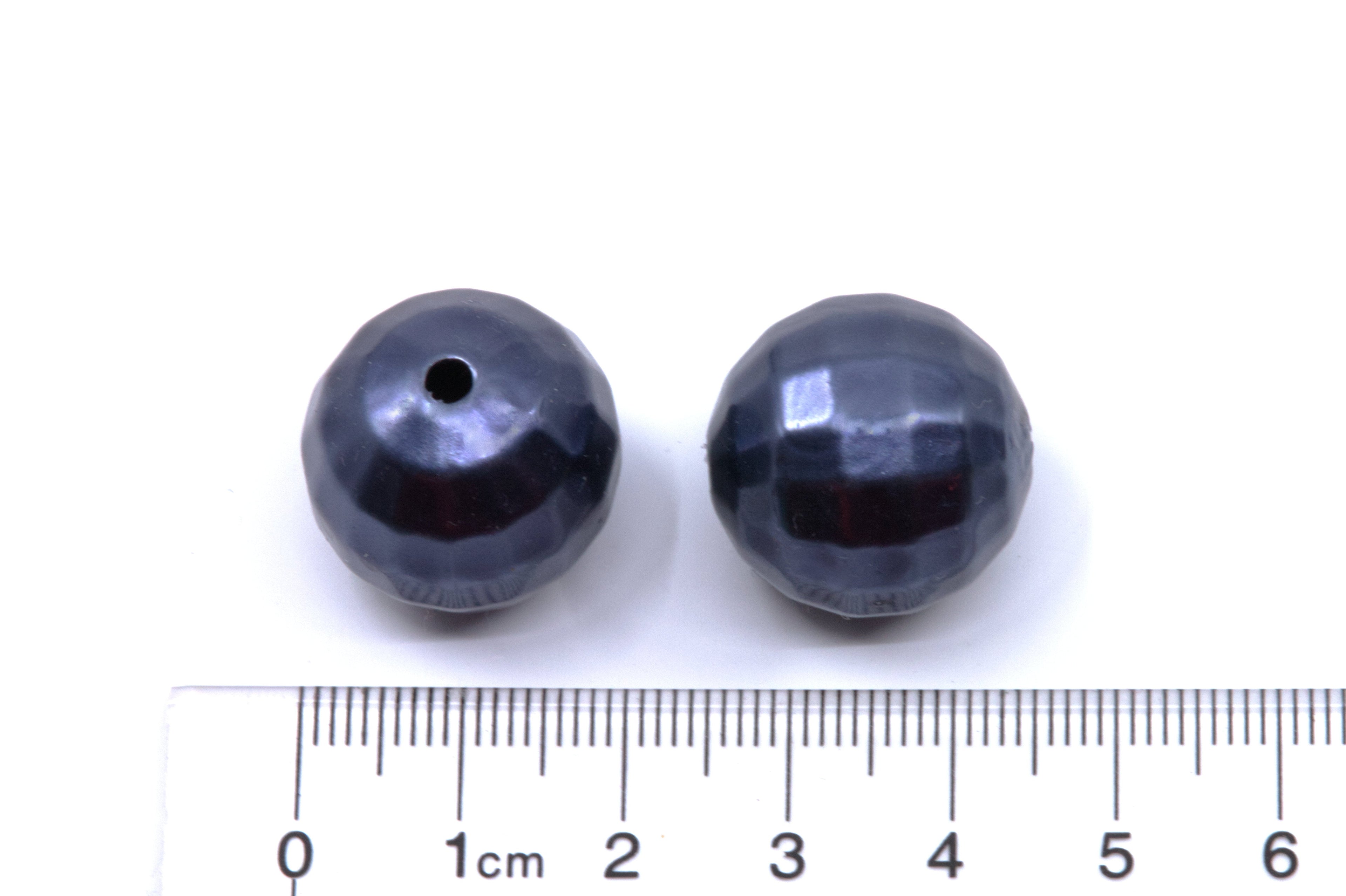 Two faceted dark blue bubblegum beads with a central hole, shown next to a white ruler for scale on a white background.