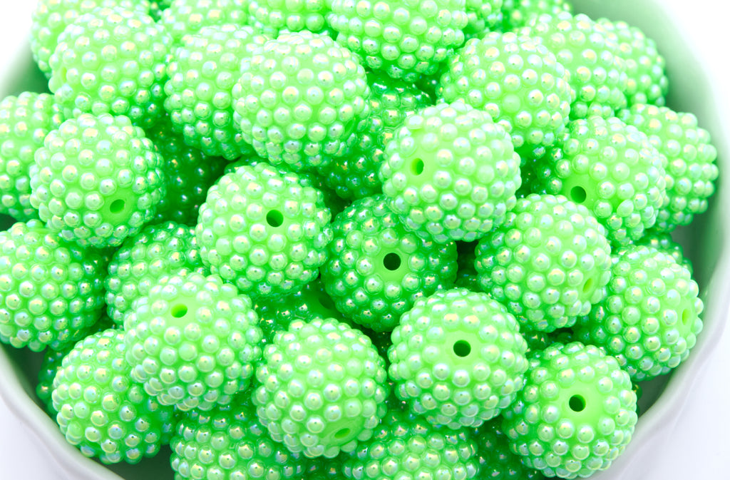 A close-up of many bright lime green beaded round craft beads piled together in a white bowl against a white background.